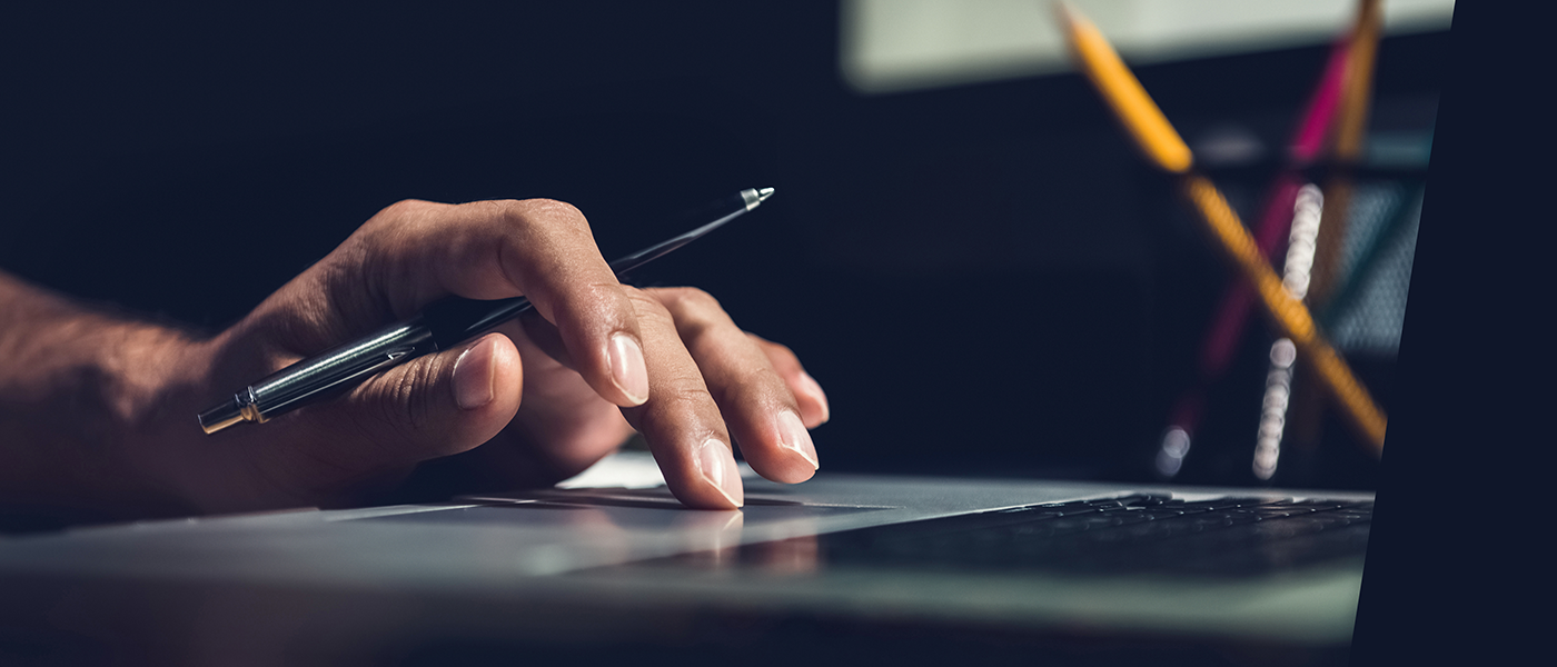 a Black person's hand is typing on a laptop keyboard as they hold a pen