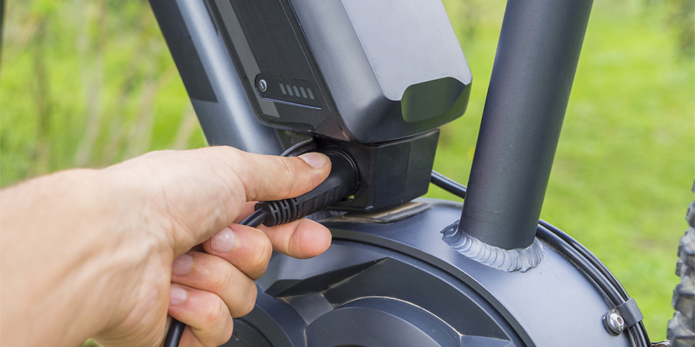 Image of a person's hand plugging in a charging adapter into a e-bike